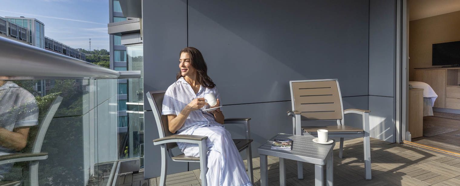 A woman enjoys a coffee on her balcony while taking in the view of Ithaca