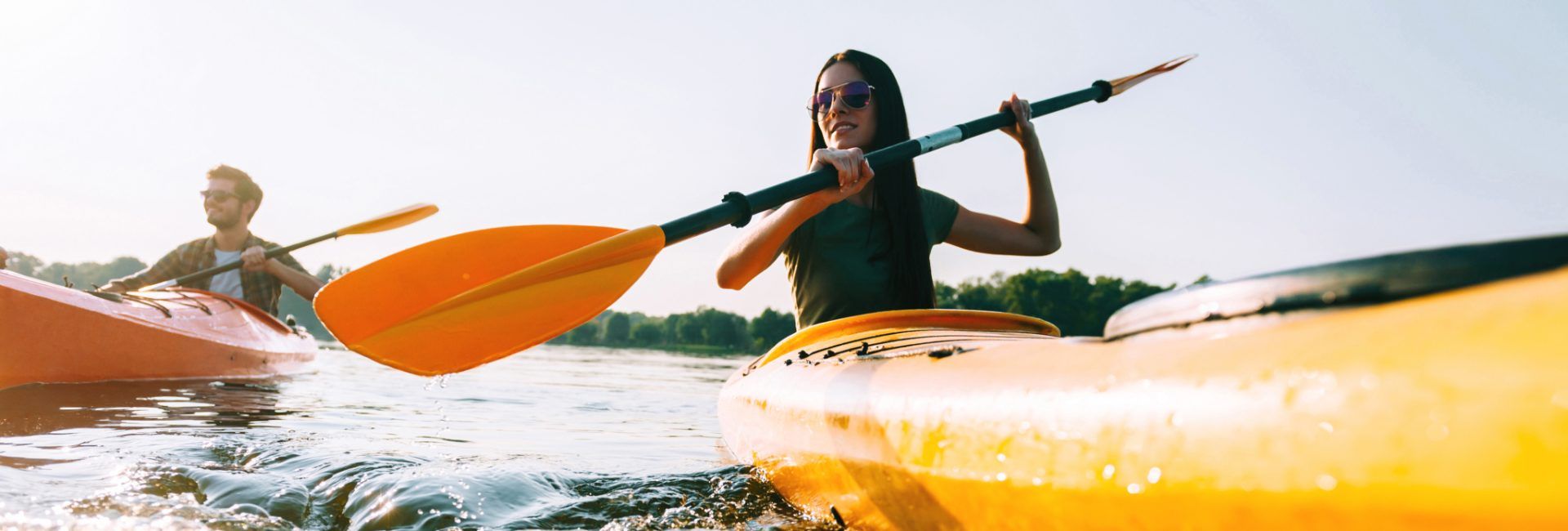 Woman in foreground paddling orange kayak, man in background also paddling a similar kayak