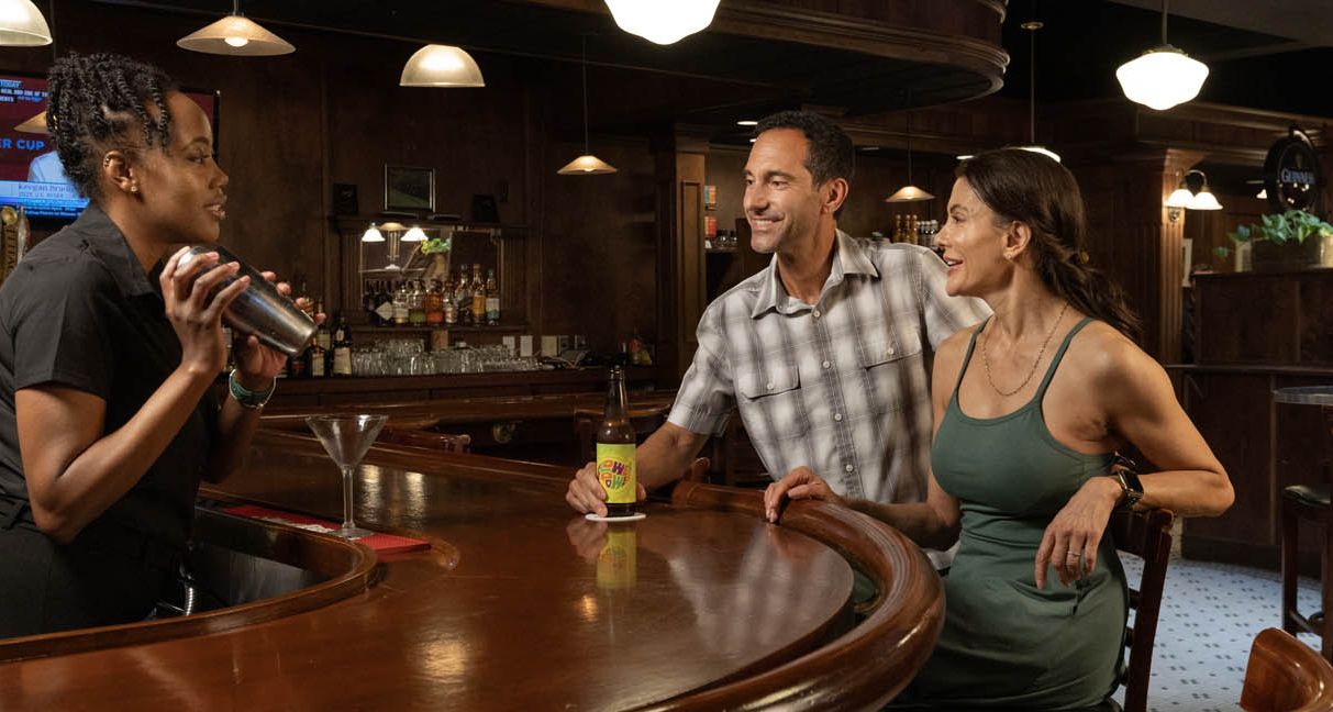 A couple enjoys a beer while chatting with a bartender who is shaking a martini