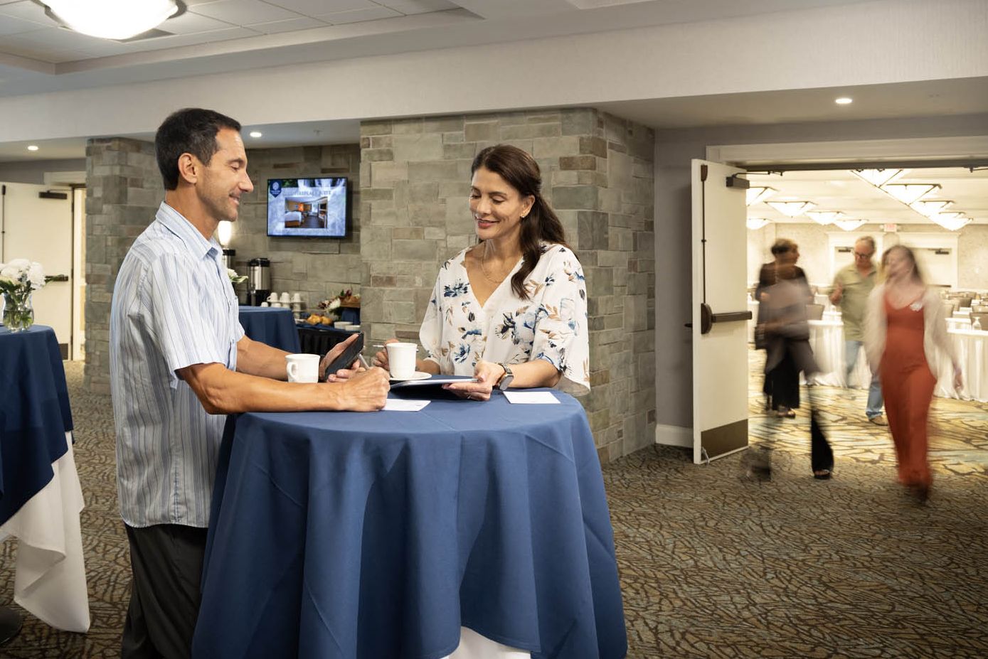 Two colleagues reviewing notes while others enter a large meeting room