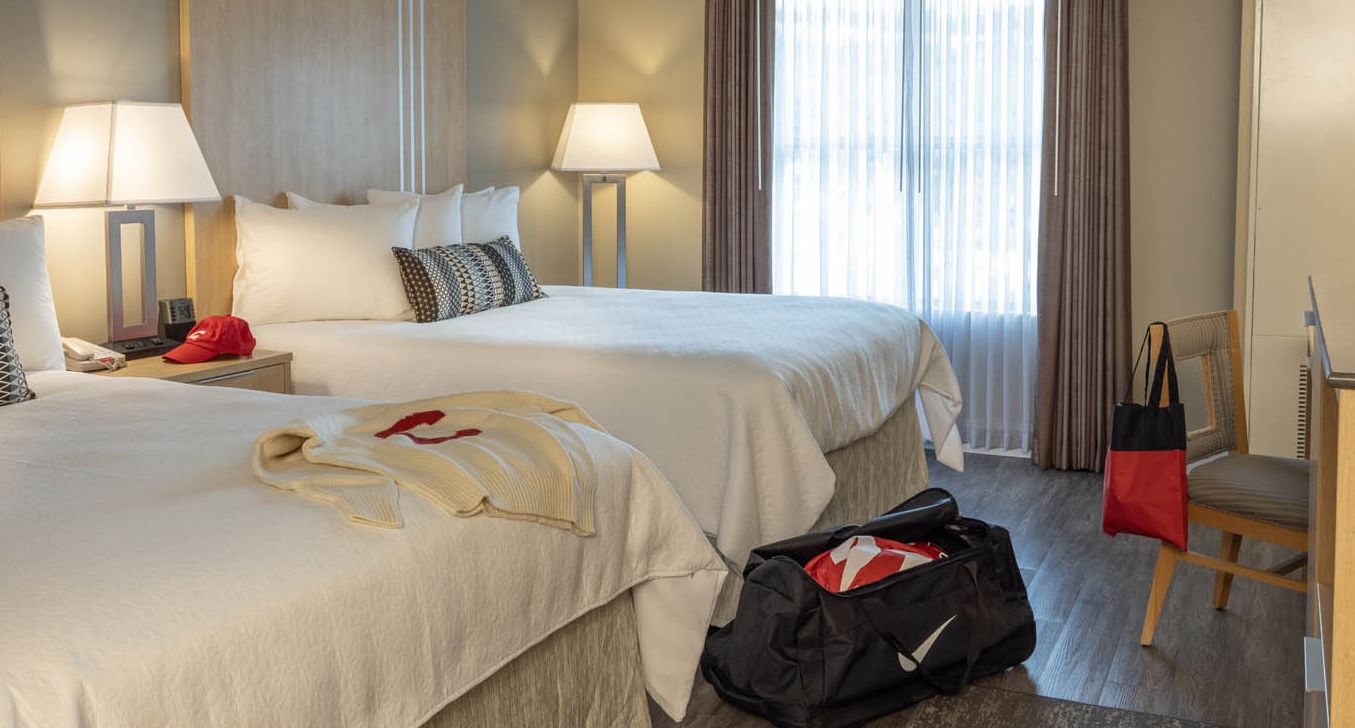 A double queen room with Cornell University gear visible on the bedspread